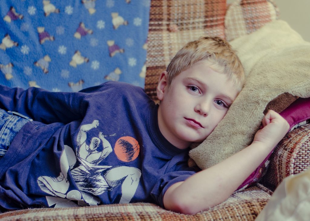 Blady blond chłopczyk, ubrany w niebieską koszulkę z białym wzorem leży na kanapie