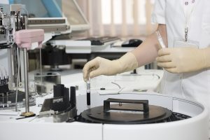 Ręka laboratnki wkłada probówkę z krwią do urządzenia w laboratorium pełnym sprzętów