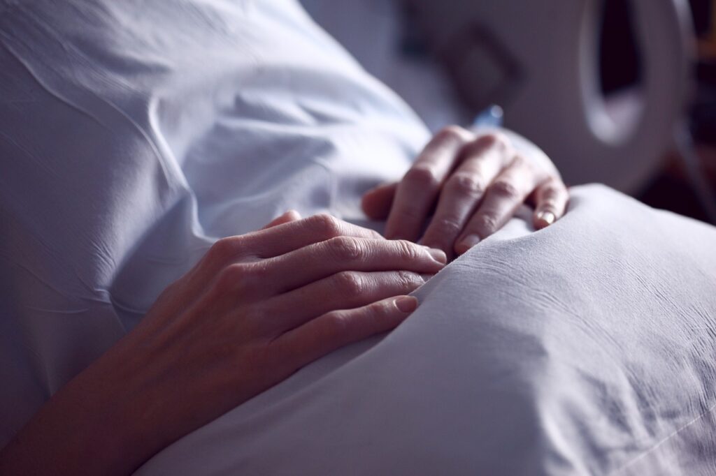 osoba chora na łóżku szpitalnym, widoczne tylko dłonie i przedramiona na szpitalnej pościeli